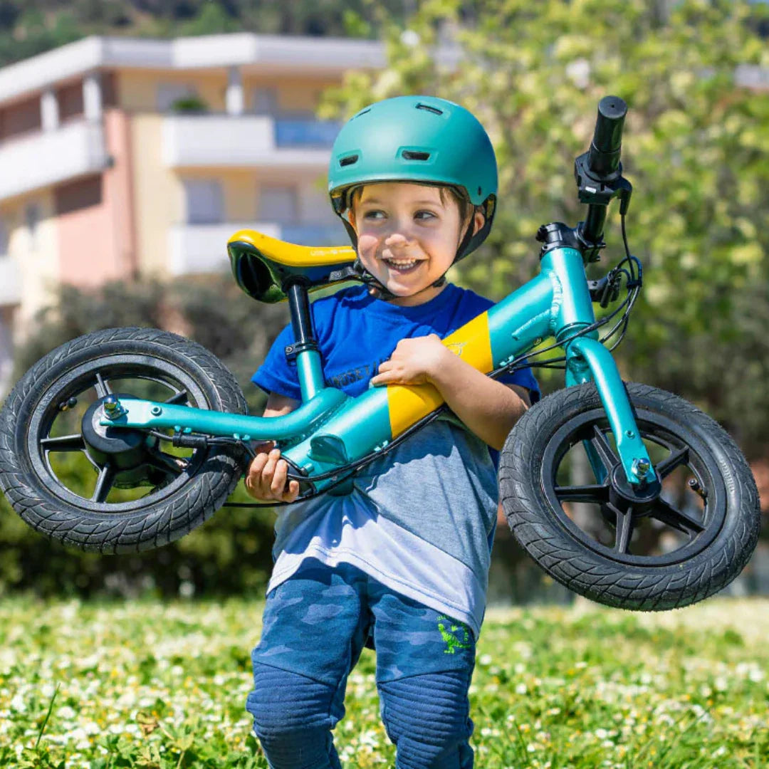 Dijete drži električnu guralicu Fiido Kidz tirkizno-žute boje u prirodi