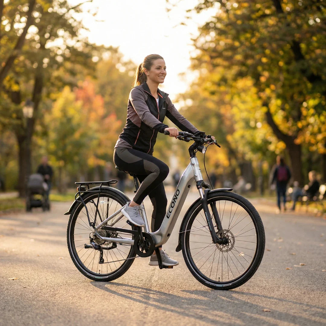 Žena vozi srebrni električni bicikl Econo Apes City EER4 2026 u parku tijekom sunčanog dana