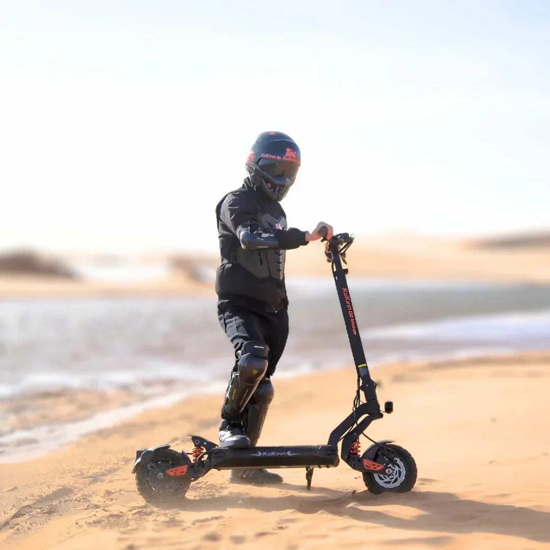 Električni romobil KuKirin G2 Master 2025 na pješčanoj plaži uz vozača s kacigom i zaštitnom opremom