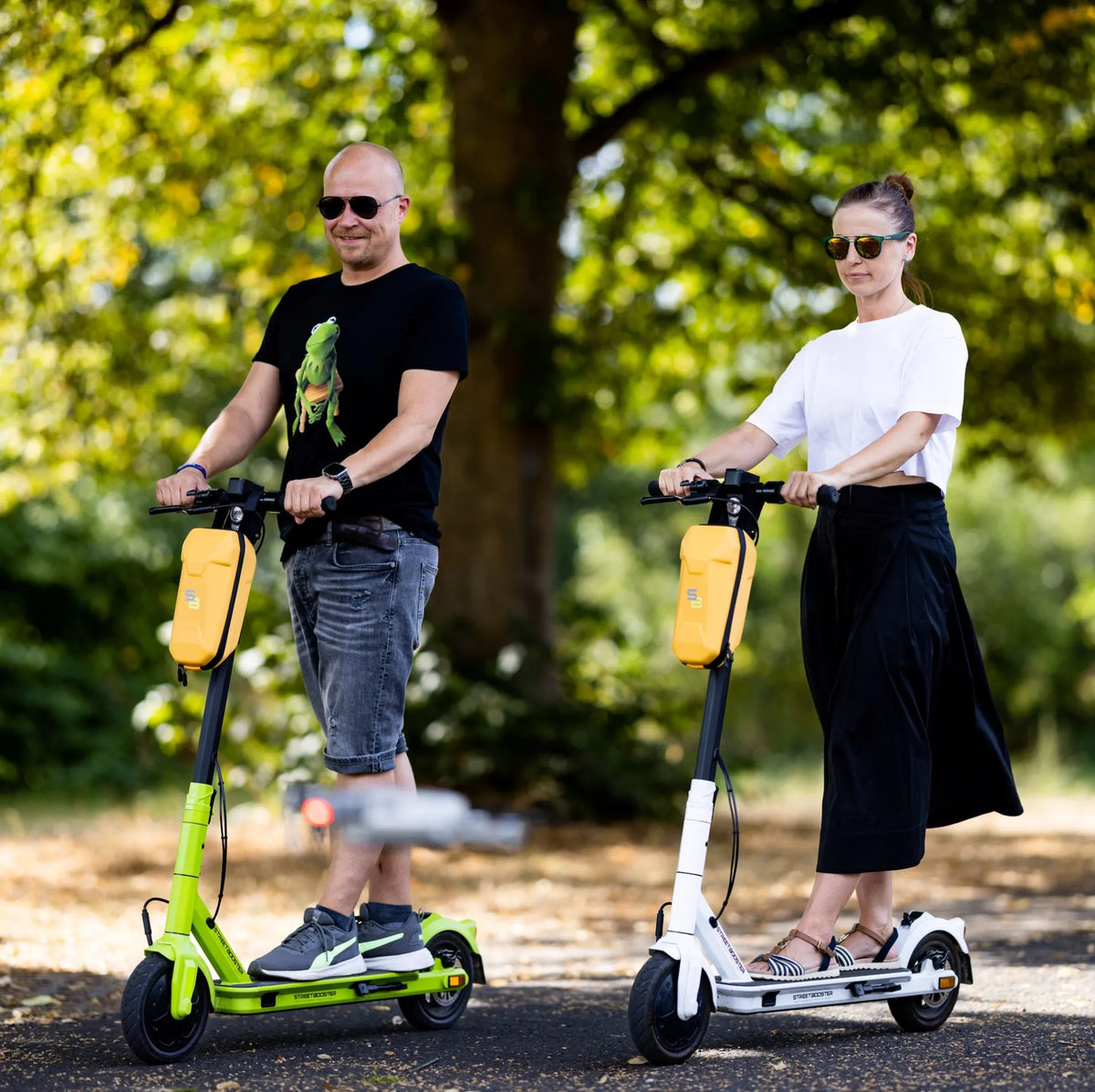 Muškarac i žena voze električni romobil Streetbooster Vega u zelenoj i bijeloj boji u parku