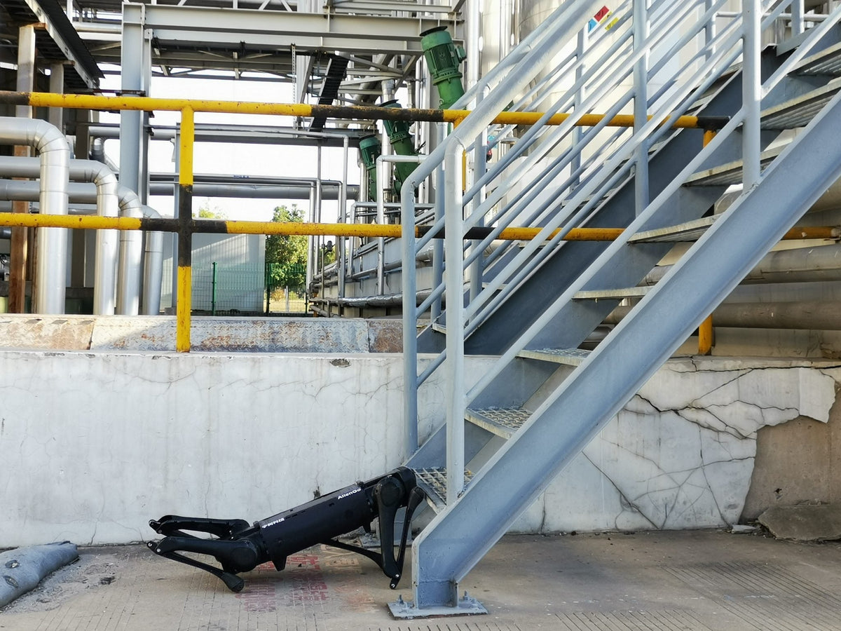 Četveronožni robot Unitree Aliengo crne boje stoji pokraj metalnih stepenica u industrijskom pogonu