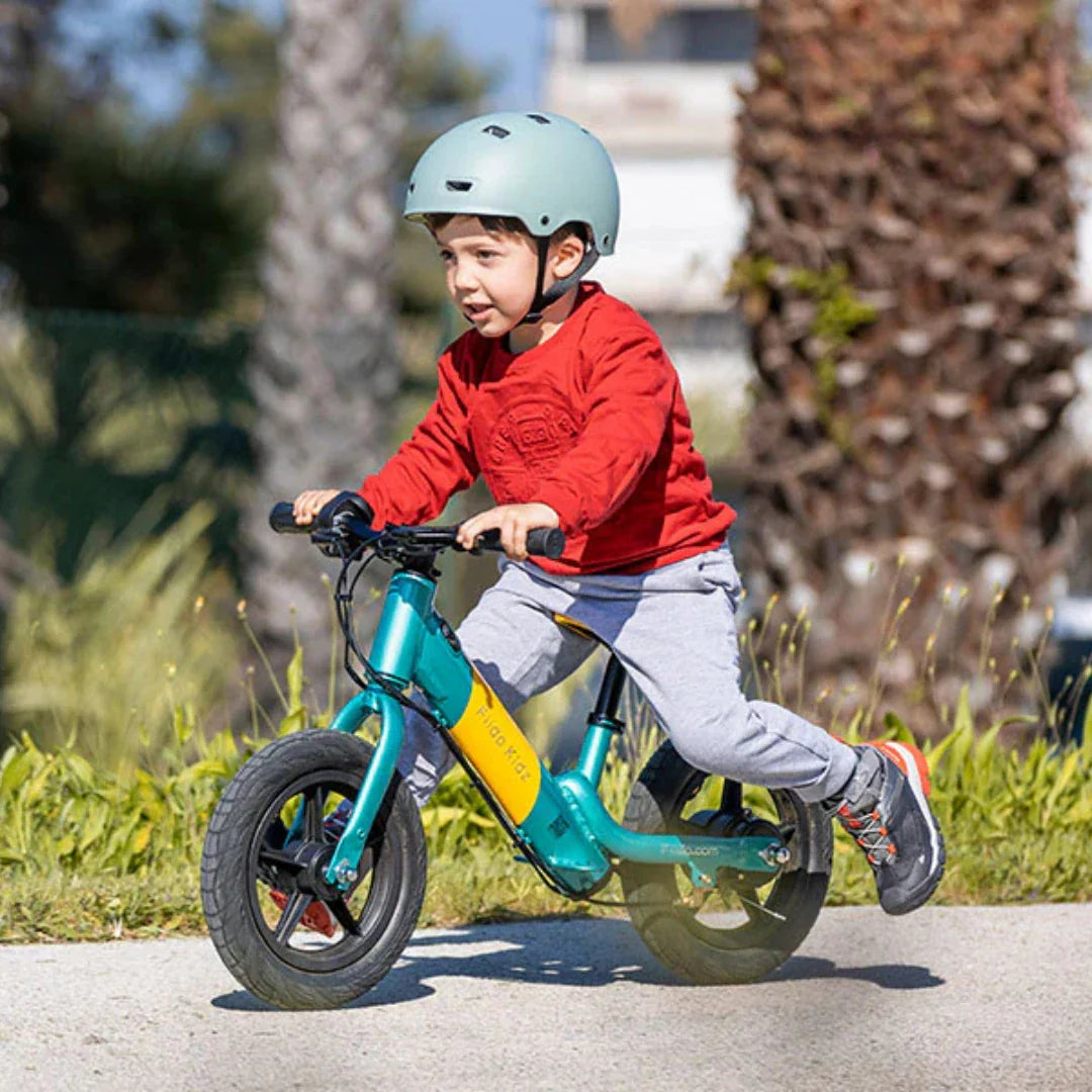 Dijete vozi plavo-žutu električnu guralicu Fiido Kidz s kacigom na glavi u prirodi
