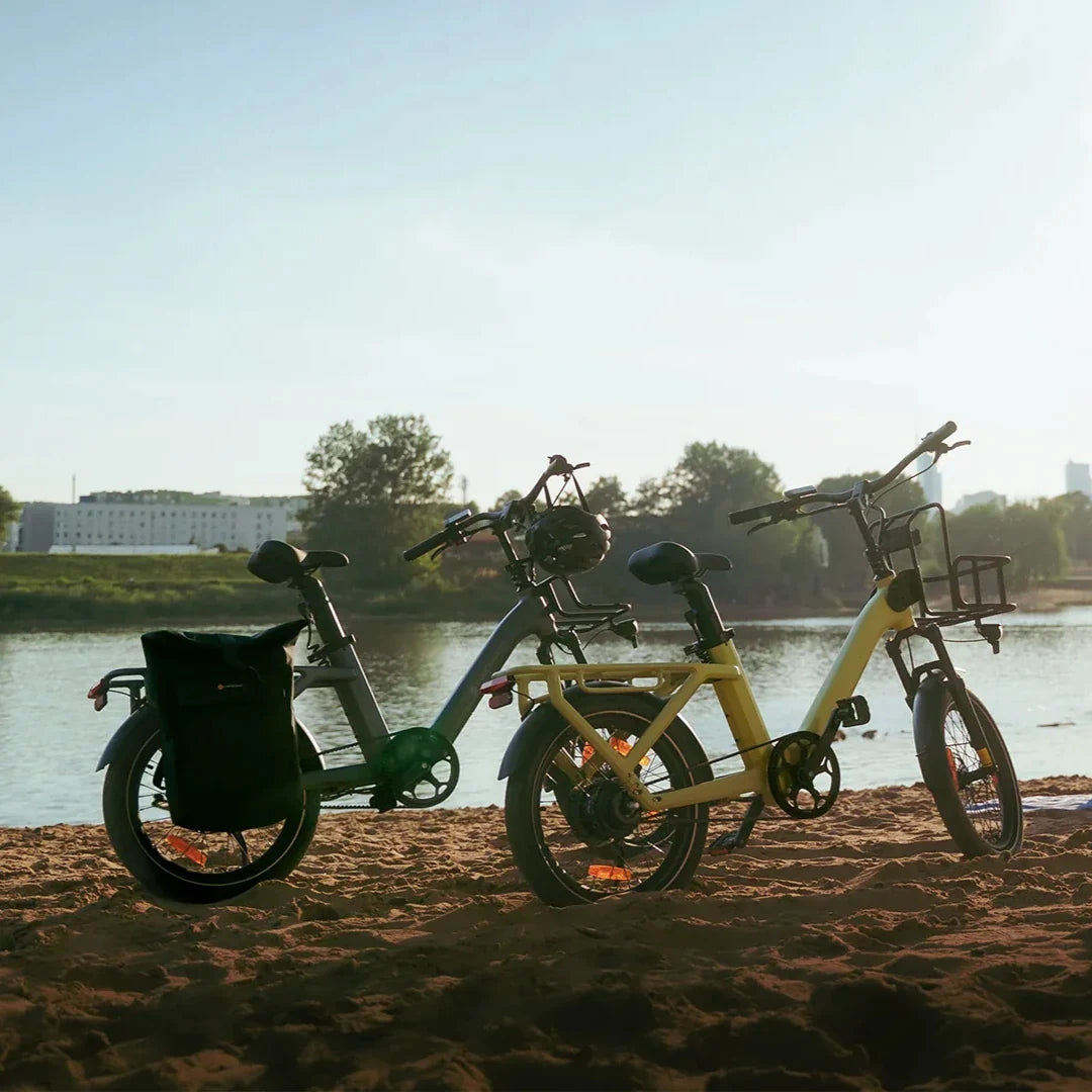 Dva električna bicikla ADO Air 20 Pro u sivoj i žutoj boji parkirana na pješčanoj plaži uz rijeku