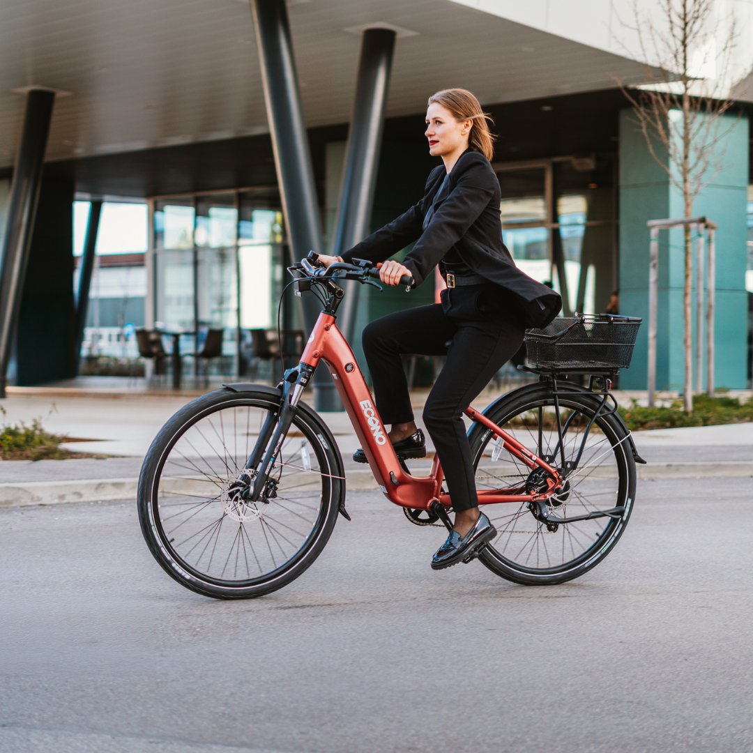Poslovna žena vozi crveni električni bicikl Econo Apes EER4 ispred moderne zgrade, profilni prikaz