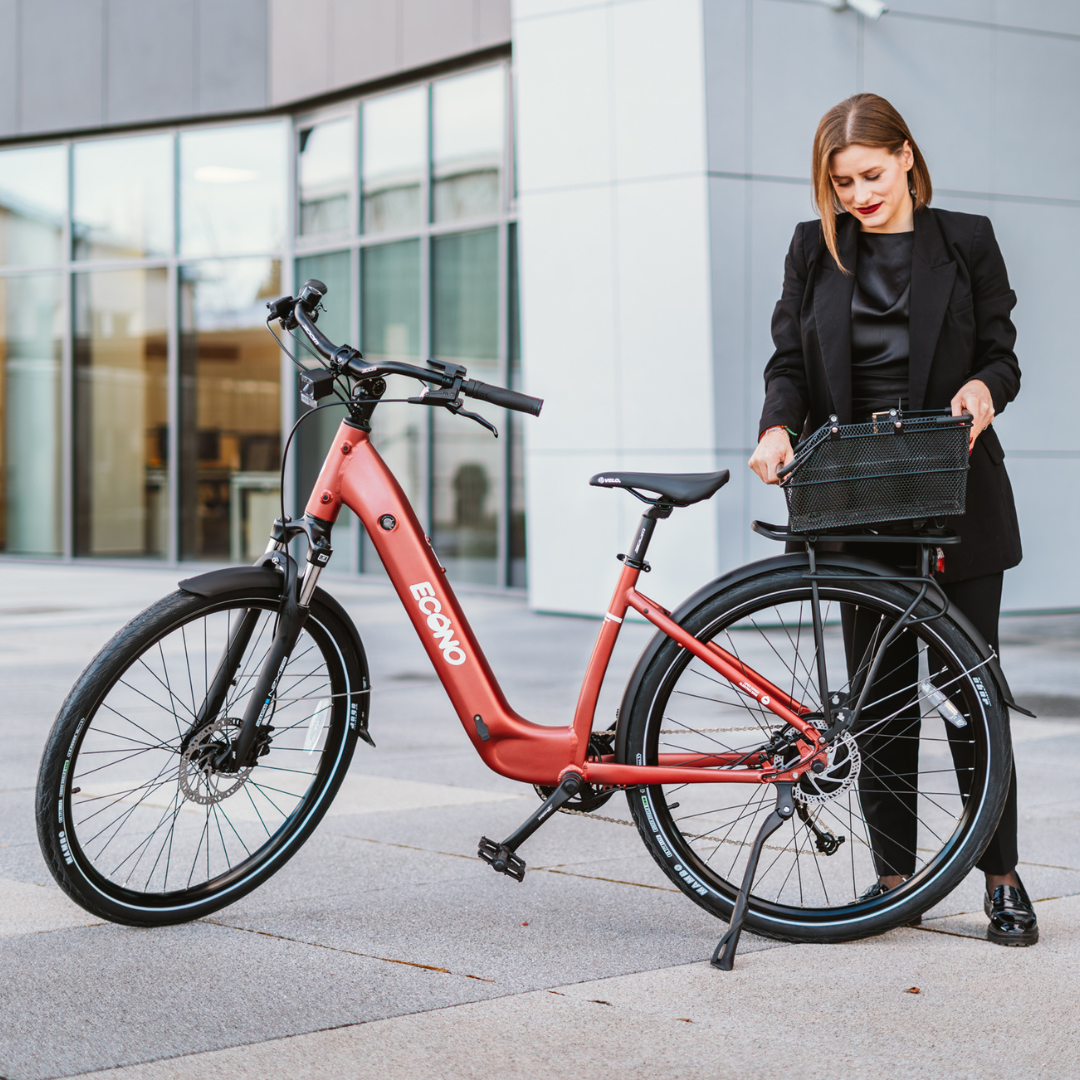 Crveni električni bicikl Econo Apes EER4 s košarom i poslovna žena ispred moderne zgrade