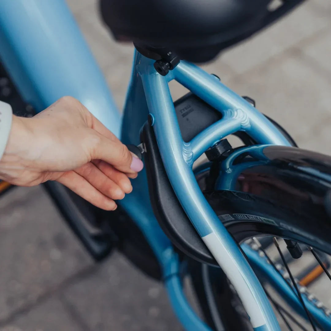 Ruka otključava bateriju na plavom električnom biciklu Econo Mare City EEC4LK, detalj okvira