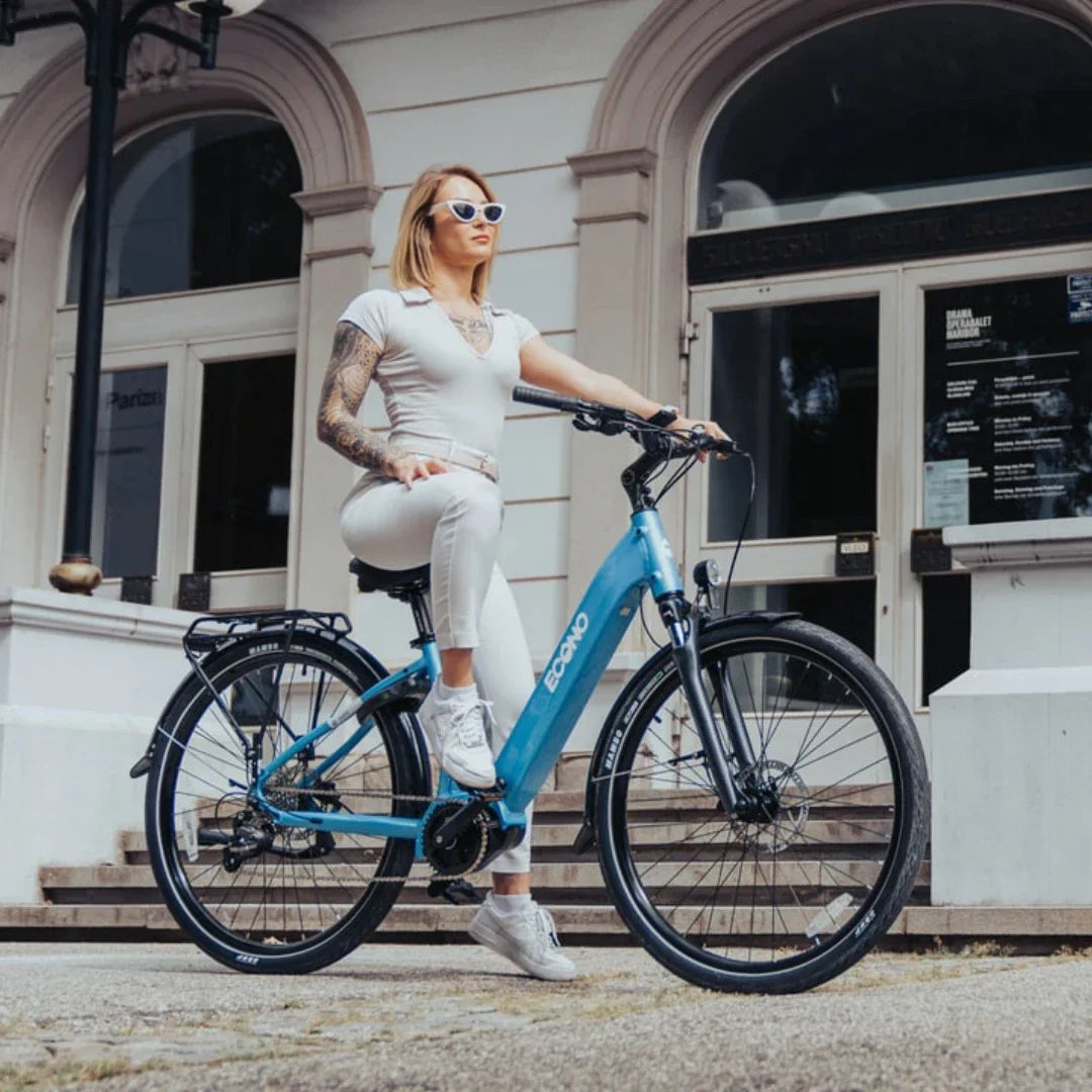 Žena sjedi na plavom električnom biciklu Econo Mare City, bočni pogled na gradskom trgu