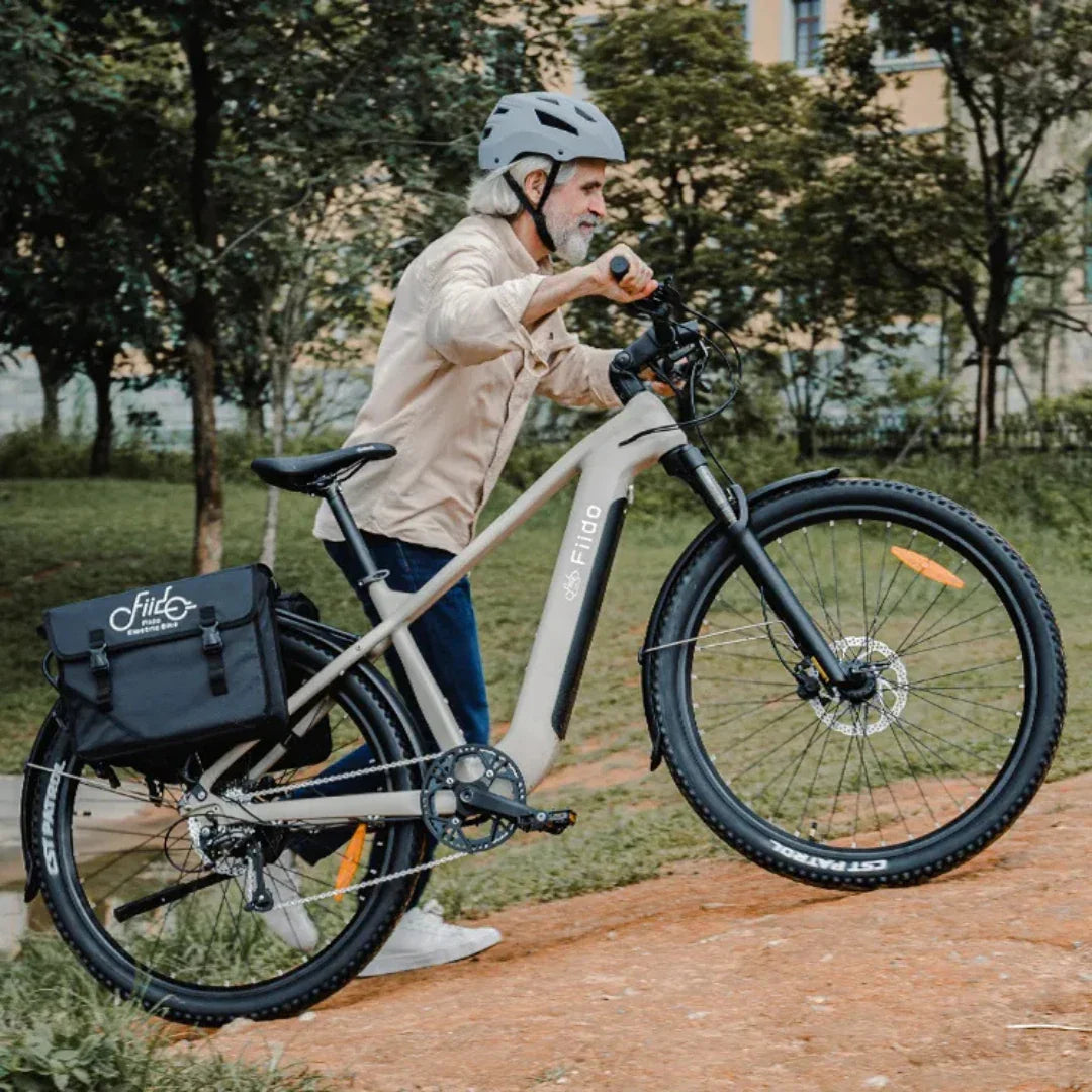 Muškarac s kacigom gura bež električni bicikl Fiido Nomads s crnom bisagom u prirodi