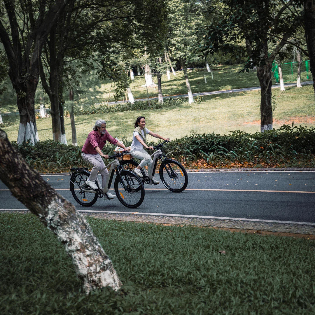 Par vozi svijetlo sivi električni bicikl Fiido Nomads kroz zeleni park po asfaltnoj cesti