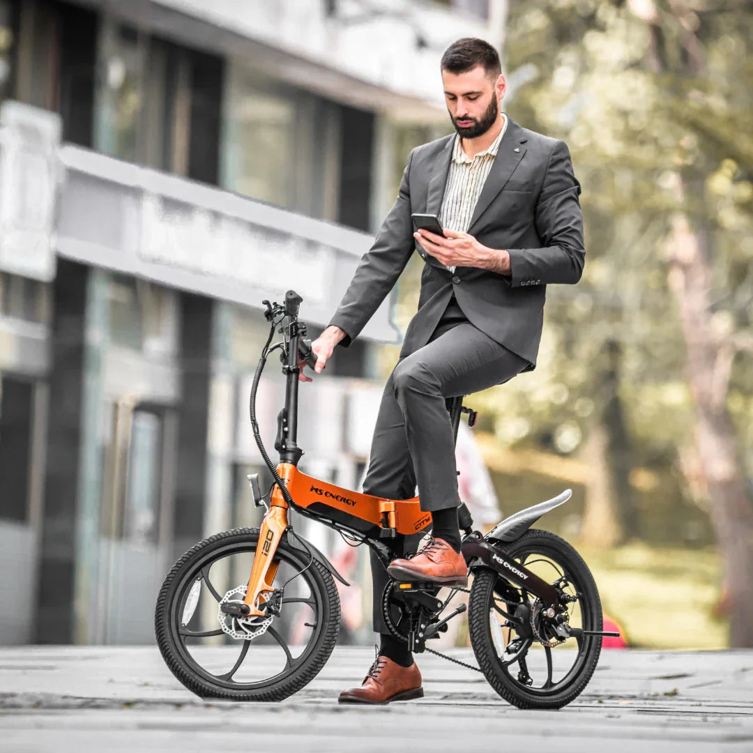 Muškarac u odijelu na narančastom električnom biciklu MS Energy i20 u gradskom okruženju
