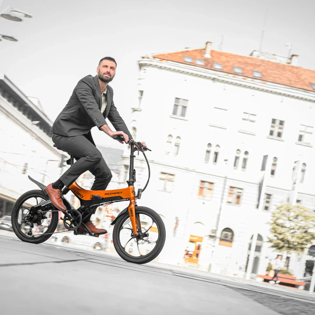 Muškarac u odijelu vozi narančasti električni bicikl MS Energy i20 gradskom ulicom