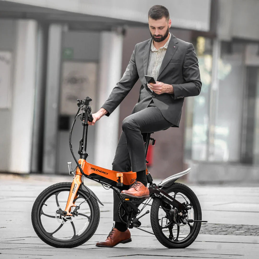 Muškarac u odijelu na narančastom sklopivom električnom biciklu MS Energy i20 na gradskom trgu