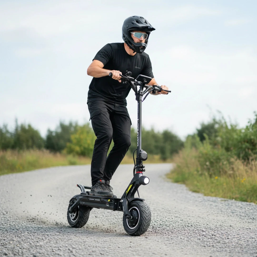 Muškarac vozi crni električni romobil Dualtron New Achilleus po šljunčanom putu bočni pogled