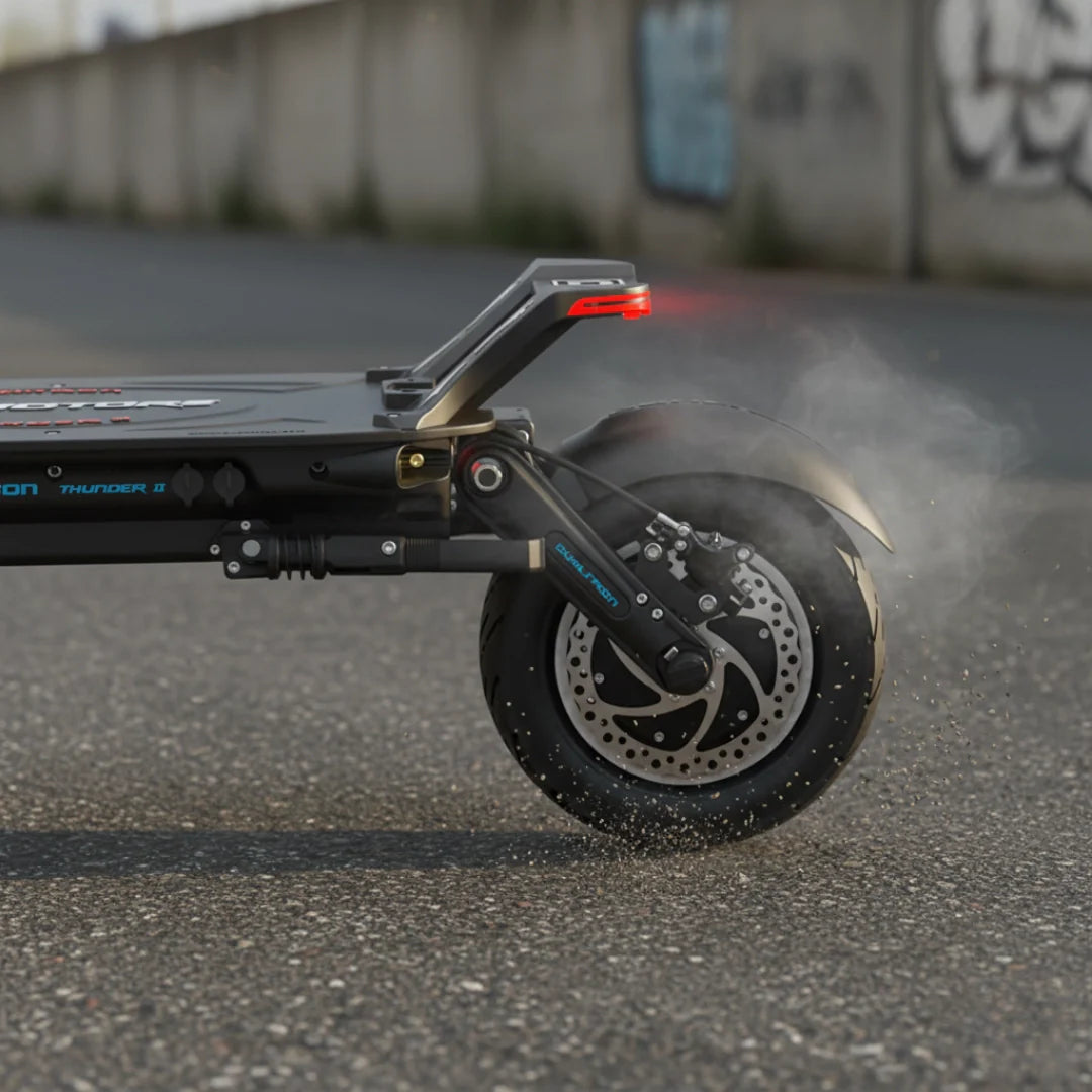 Bočni pogled na stražnji kotač i ovjes električnog romobila Dualtron Thunder 2 s dimom na asfaltu