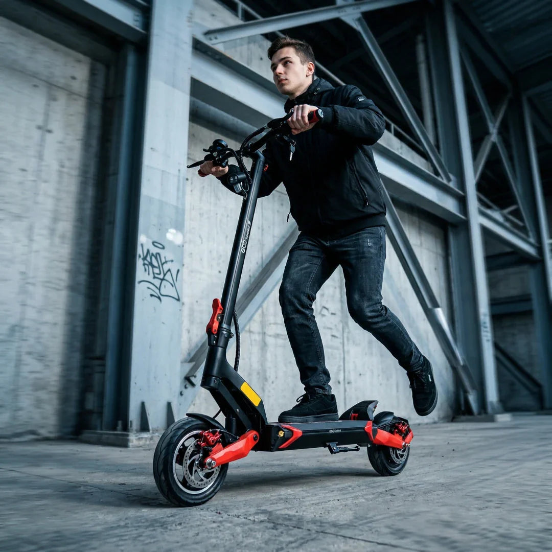 Mladić vozi crno-crveni električni romobil Eco Speed 9 u industrijskom okruženju, bočni pogled