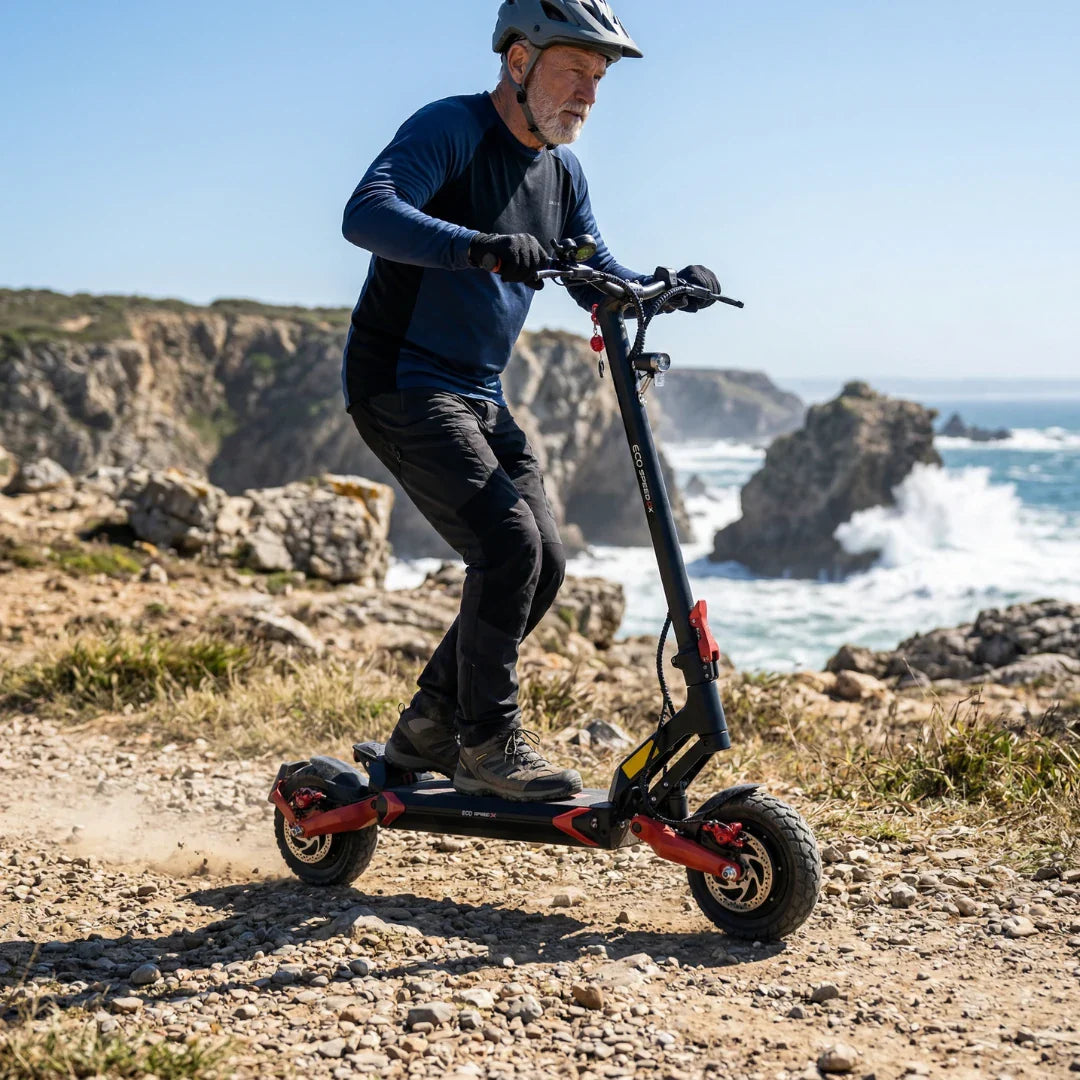 Stariji muškarac vozi crno-crveni električni romobil Eco Speed 9x na makadamskoj stazi uz more