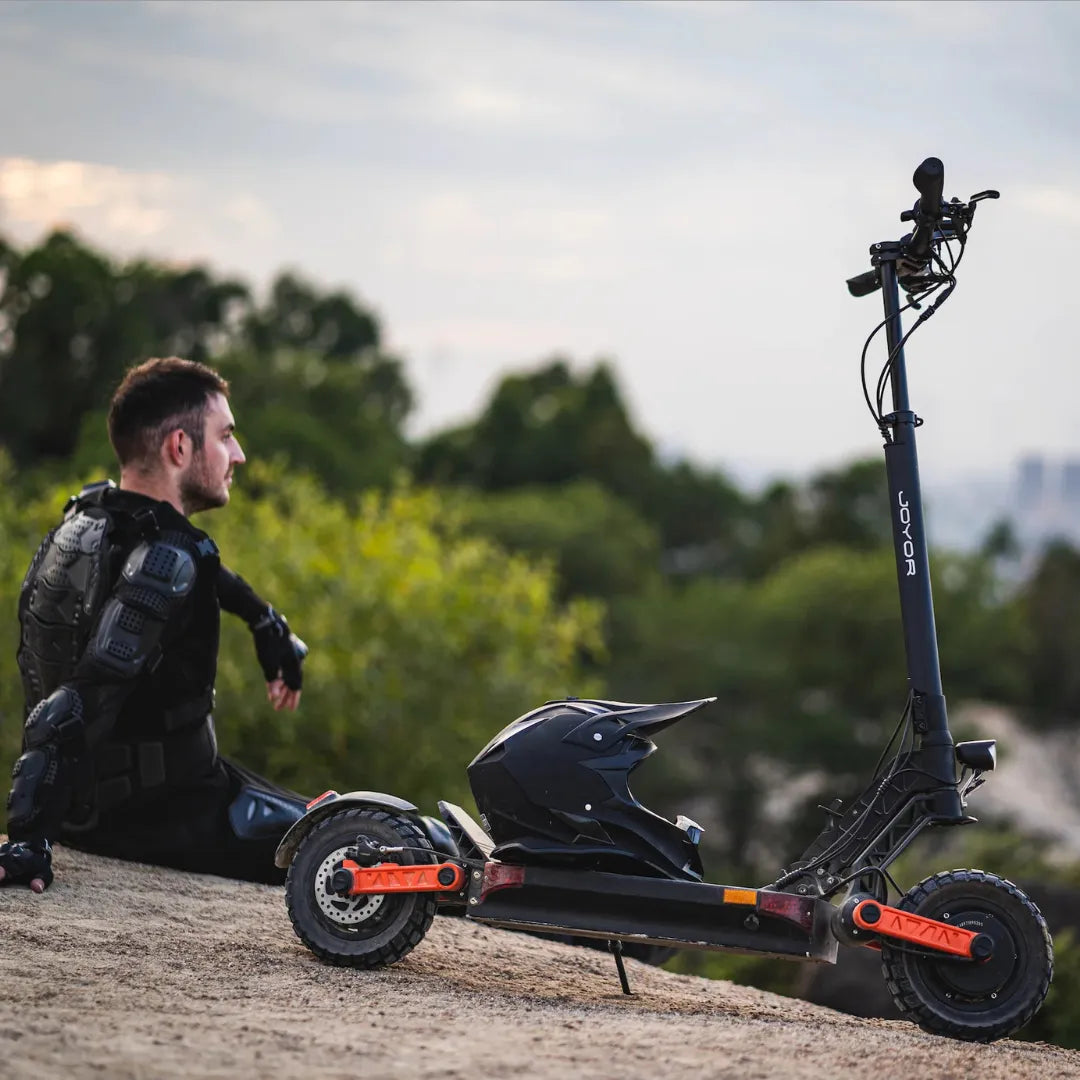 Električni romobil Joyor S10-S crne boje s narančastim detaljima i kacigom na gazištu u prirodi
