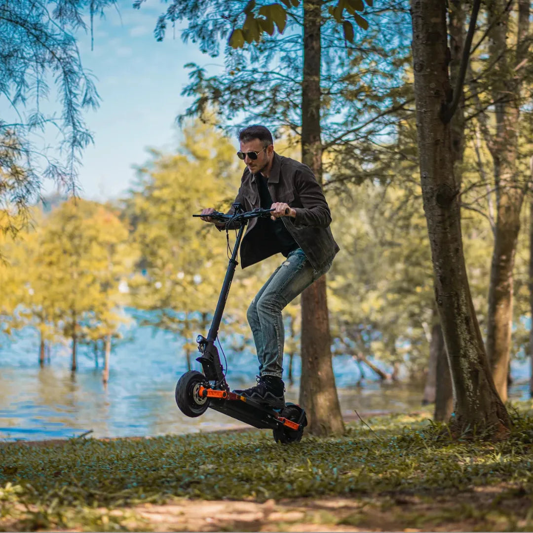 Muškarac vozi crni električni romobil Joyor S10-S s narančastim detaljima uz jezero u šumi