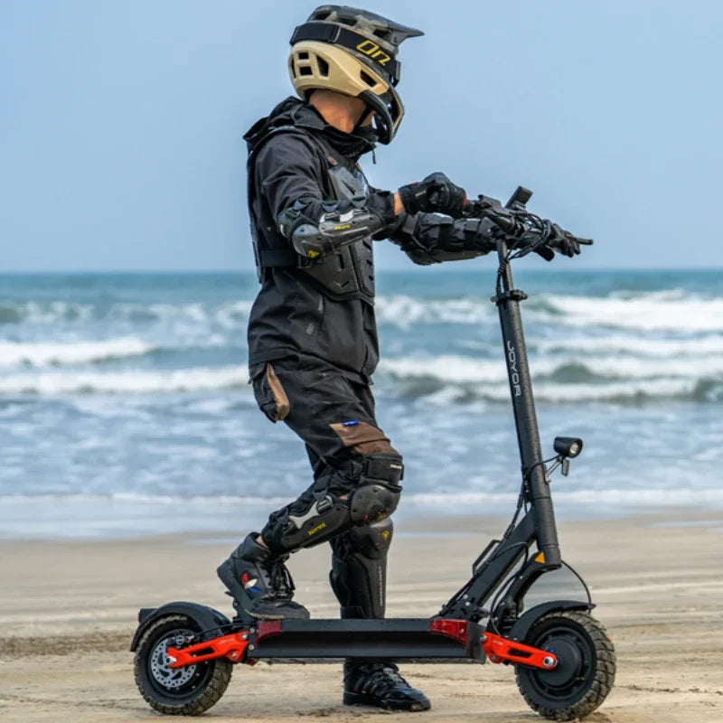 Električni romobil Joyor T10 crne boje s vozačem u zaštitnoj opremi na pješčanoj plaži bočni pogled