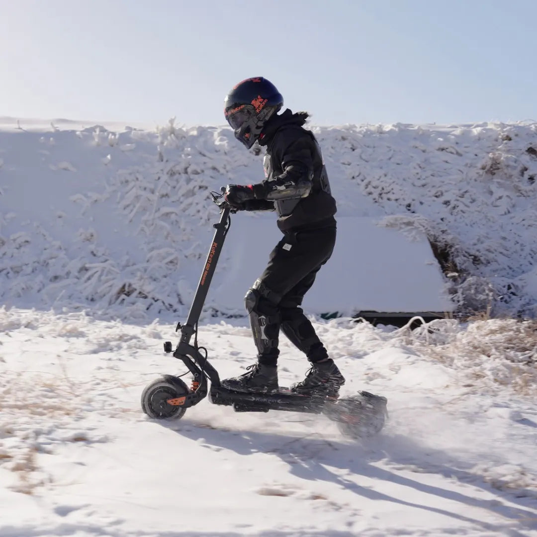 Električni romobil KuKirin G2 Master u vožnji po snijegu, pogled sa strane na crni model