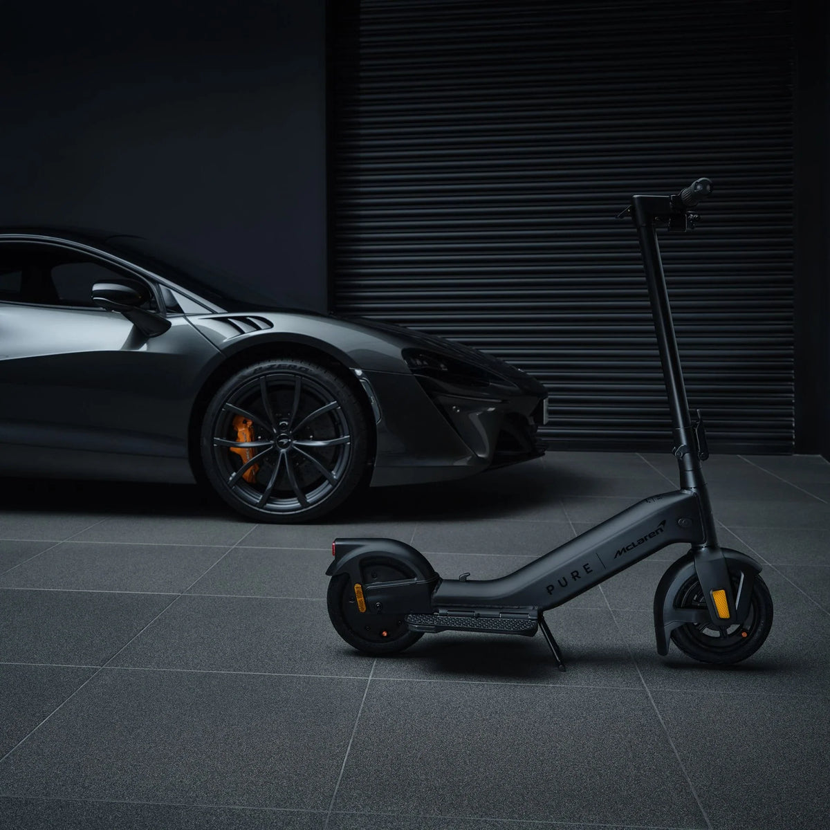 Crni električni romobil Pure Advance McLaren Edition, profilni pogled pored sportskog automobila