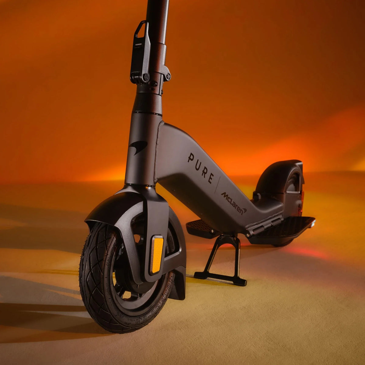Crni električni romobil Pure Advance McLaren Edition, pogled sprijeda na narančastoj podlozi