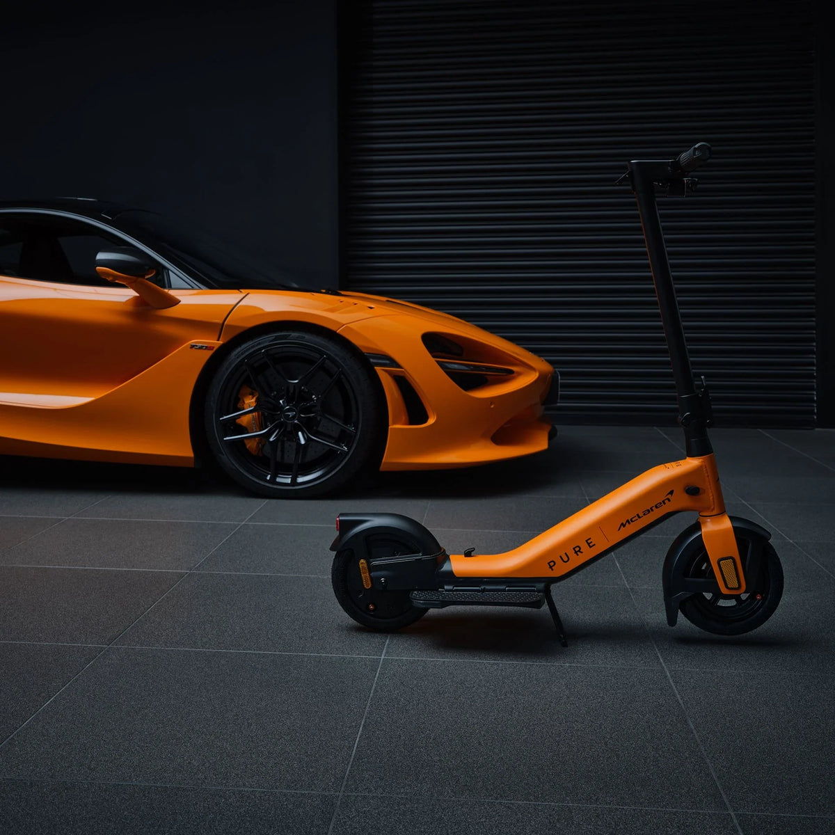 Narančasti električni romobil Pure Advance McLaren Edition parkiran pored McLaren automobila