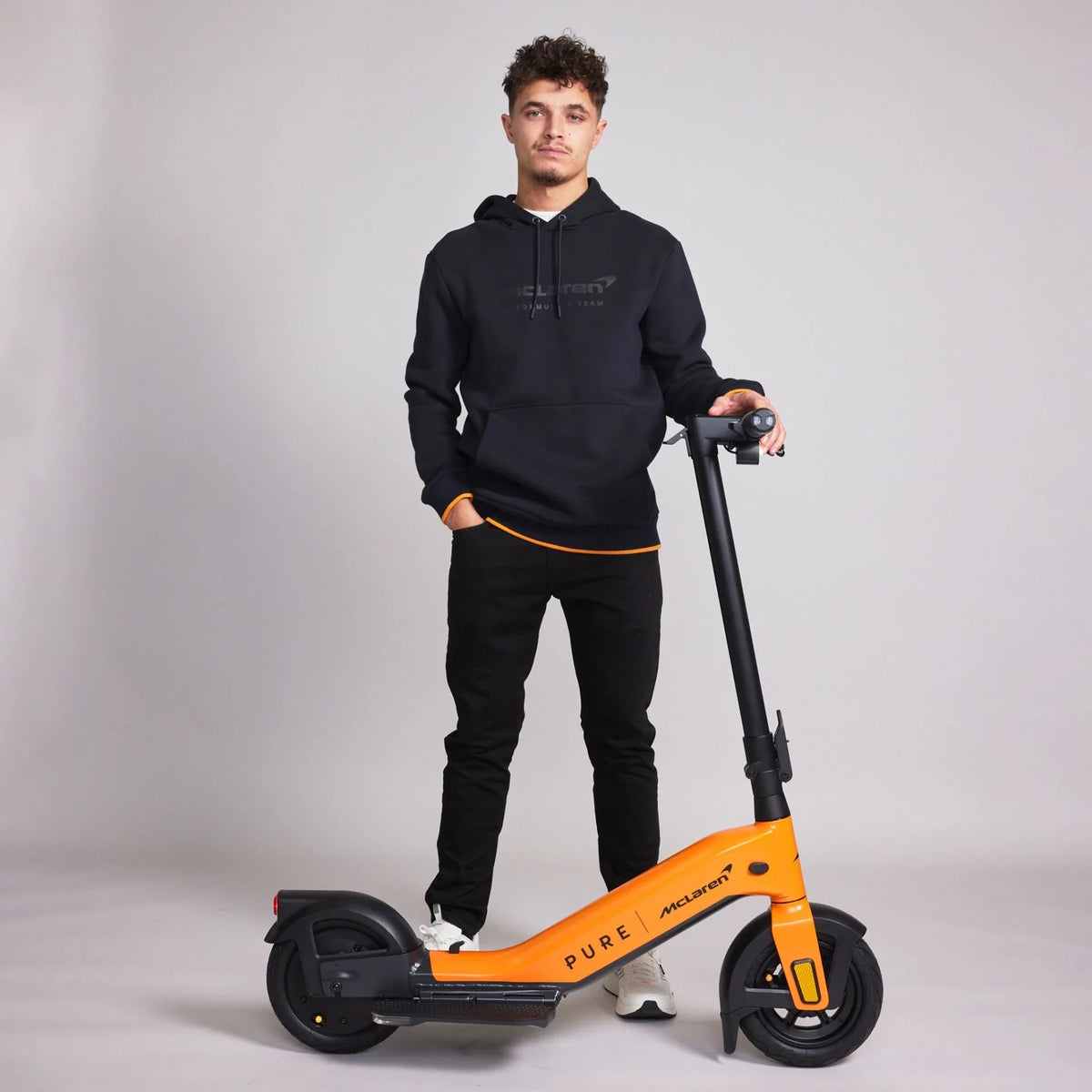 Muškarac pored narančasto-crnog električnog romobila Pure Advance McLaren Edition, bočni pogled
