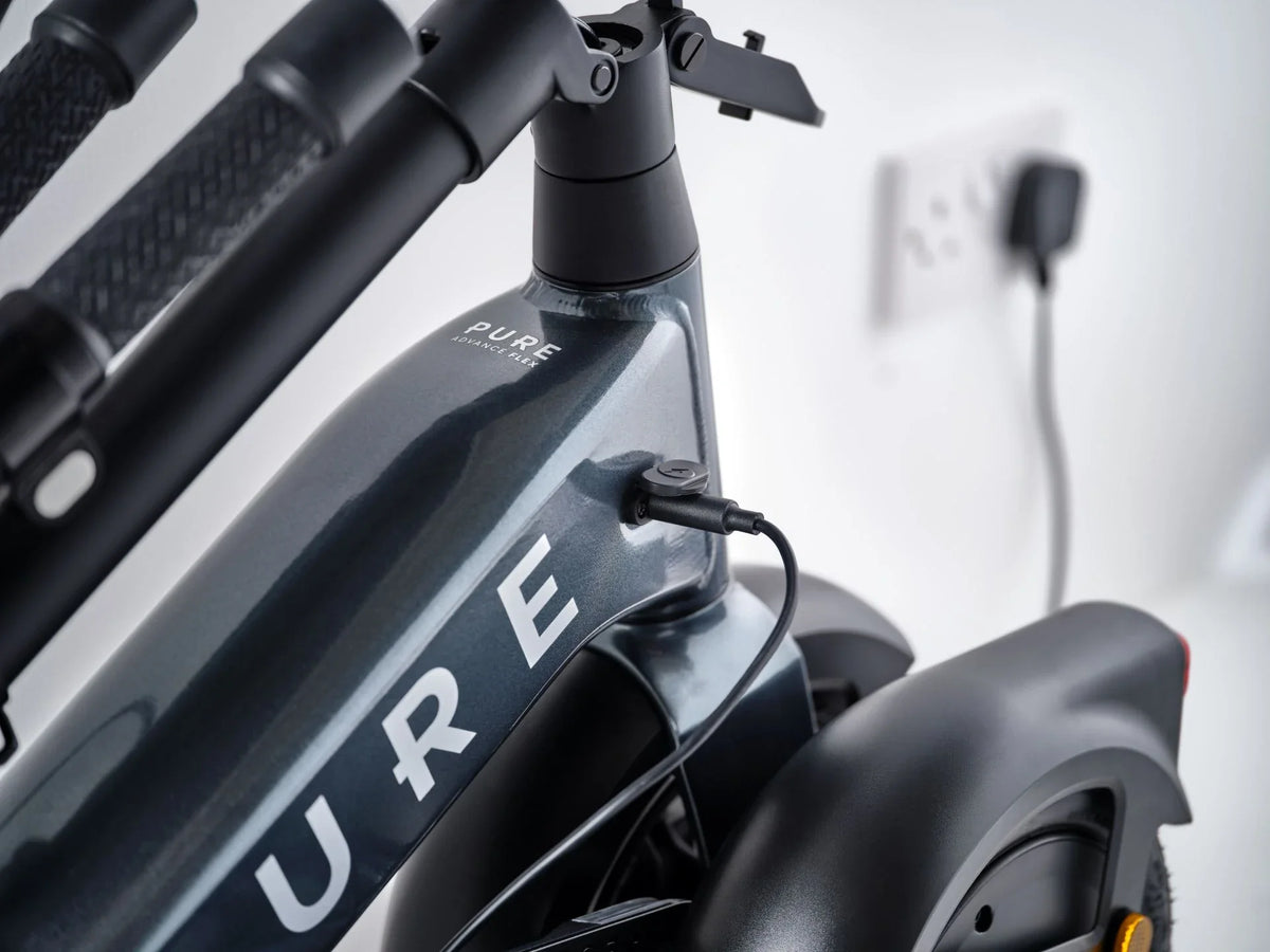 Detalj punjenja sivog električnog romobila Pure Advance Flex spojenog na utičnicu