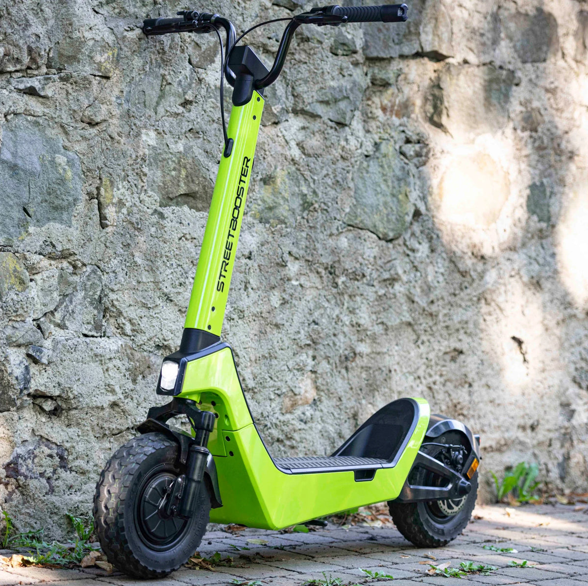 Električni romobil Streetbooster Castor svijetlo zelene boje parkiran uz kameni zid, pogled sa
