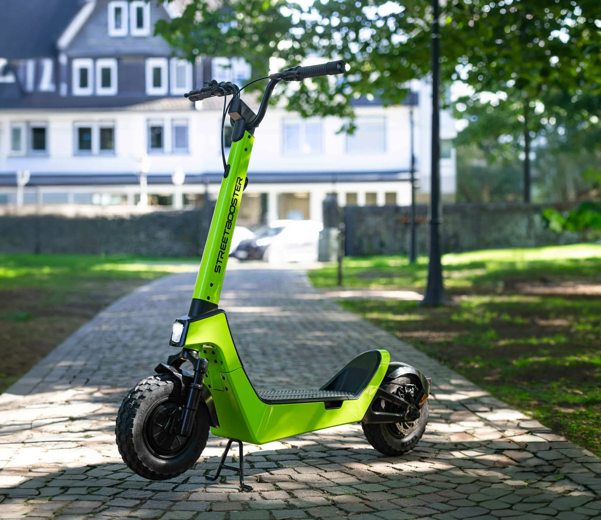 Električni romobil Streetbooster Castor svijetlo zelene boje parkiran na popločenoj stazi u parku