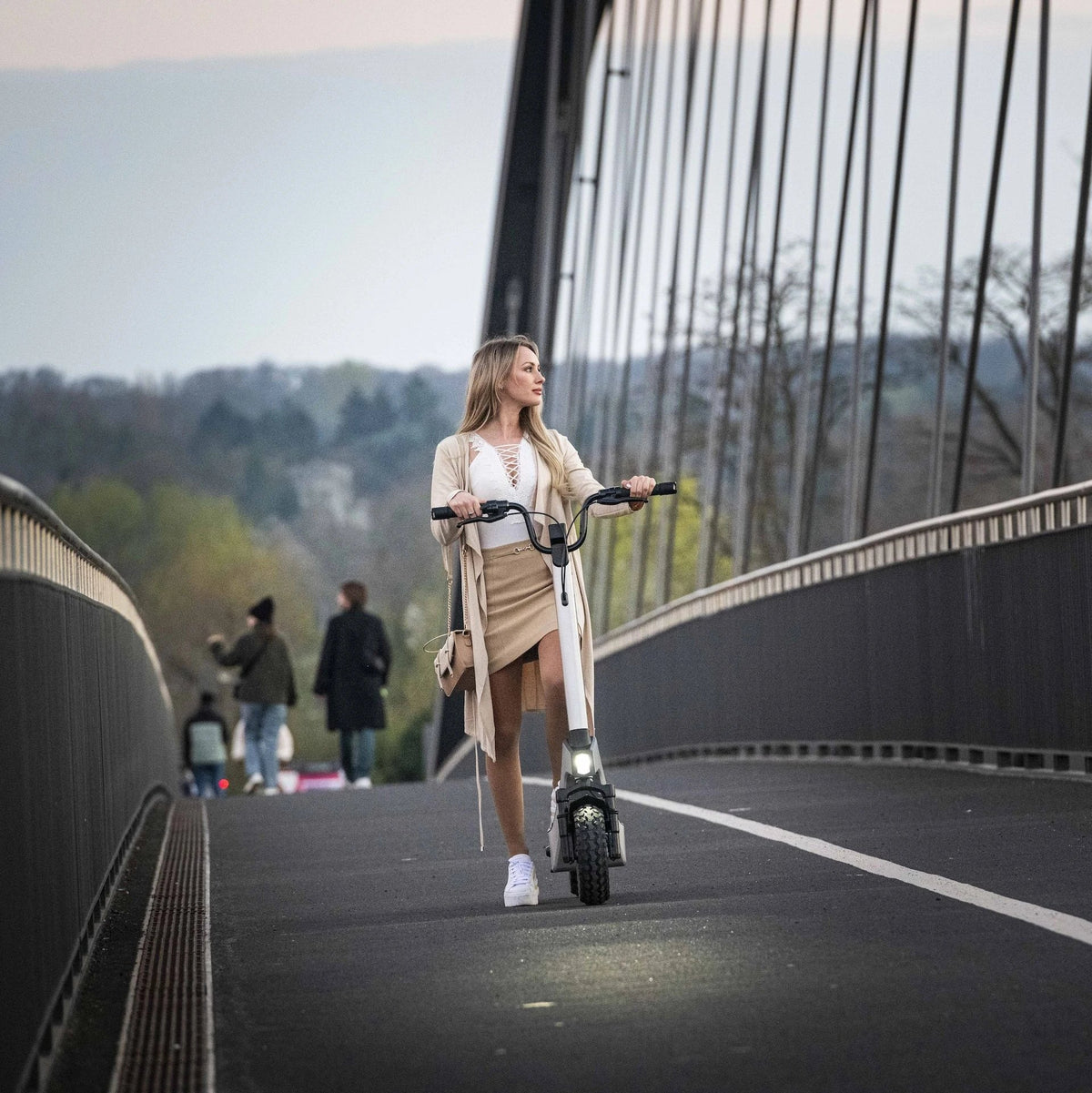 Žena vozi bijeli električni romobil Streetbooster Pollux na pješačkom mostu