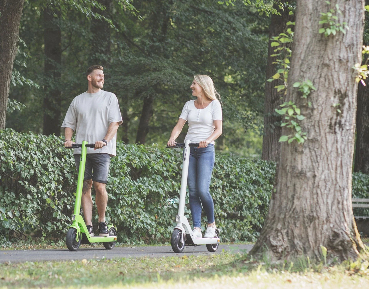 Muškarac i žena voze zeleni i bijeli električni romobil Streetbooster Sirius u parku