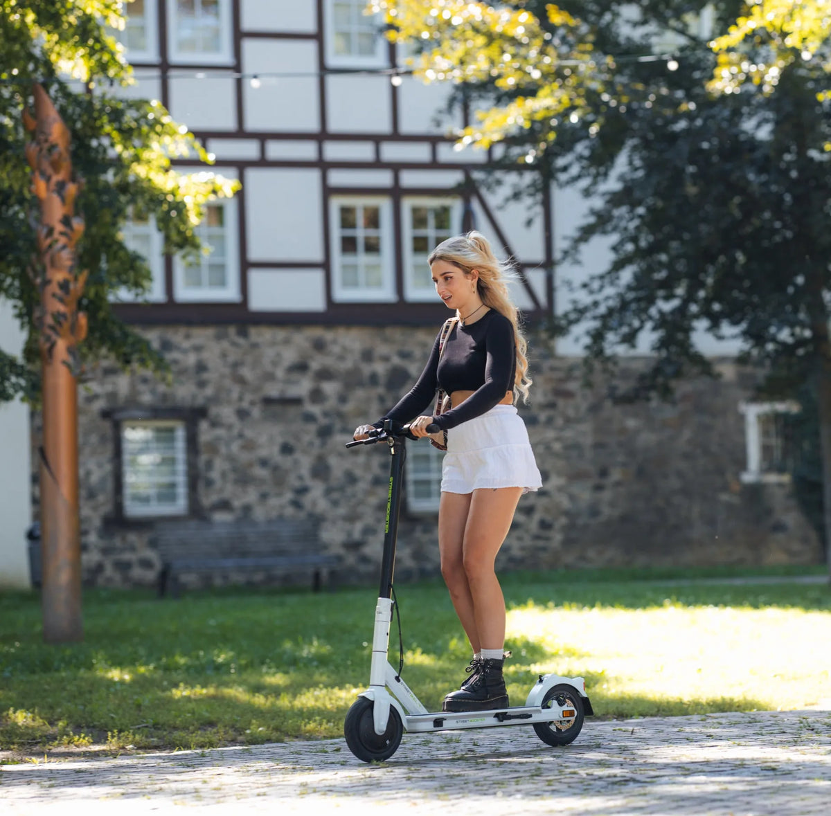 Djevojka vozi bijeli električni romobil Streetbooster Vega u parku, bočni pogled