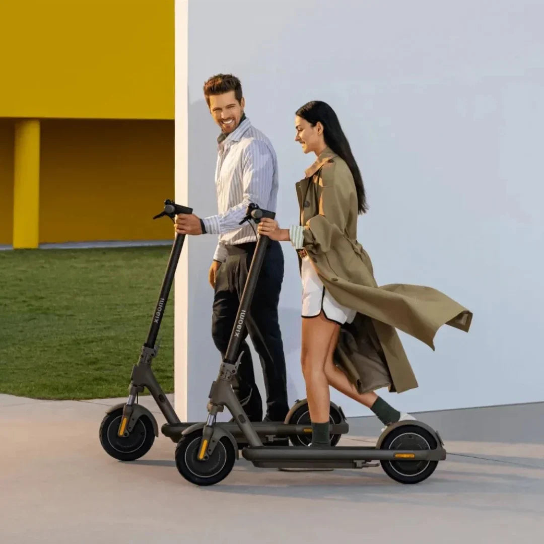 Par vozi crni električni romobil Xiaomi 5 Max GL na otvorenom uz bijeli zid