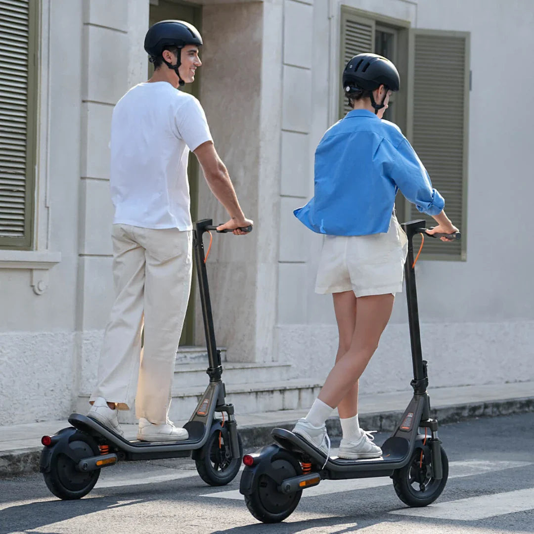 Par muškarac i žena voze crne električne romobile Xiaomi 6 na ulici s kacigama na glavi