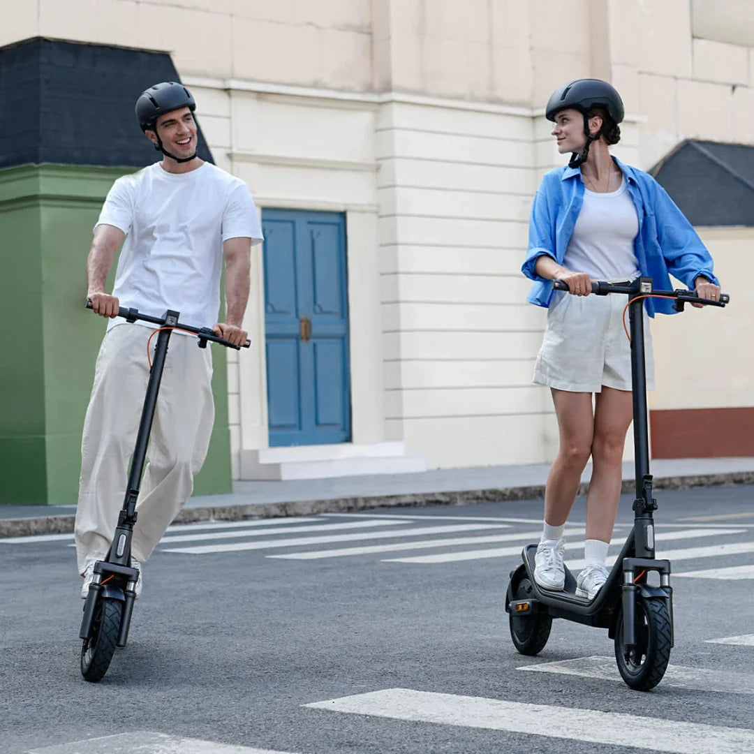 Muškarac i žena voze crni električni romobil Xiaomi 6 na cesti s kacigama na glavi