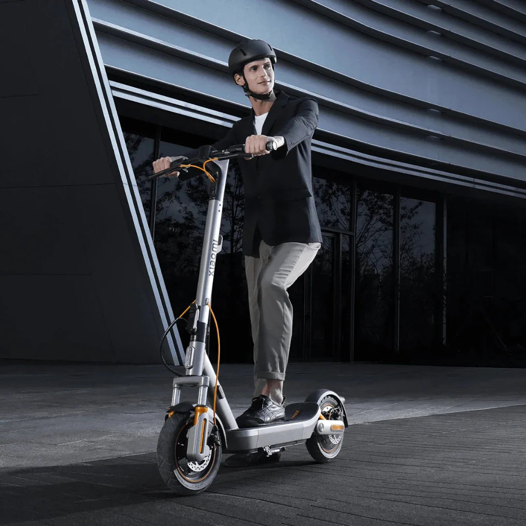 Muškarac s kacigom vozi sivi električni romobil Xiaomi 6 Max ispred moderne zgrade