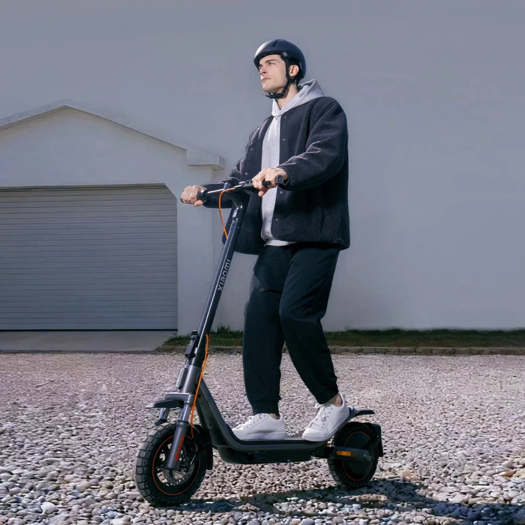 Muškarac s kacigom vozi crni električni romobil Xiaomi 6 Pro po šljunčanom putu bočni pogled