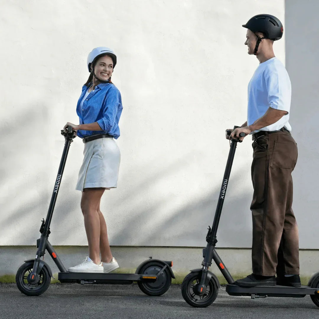 Muškarac i žena voze crne električne romobile Xiaomi Elite s kacigama na glavi, profilni prikaz