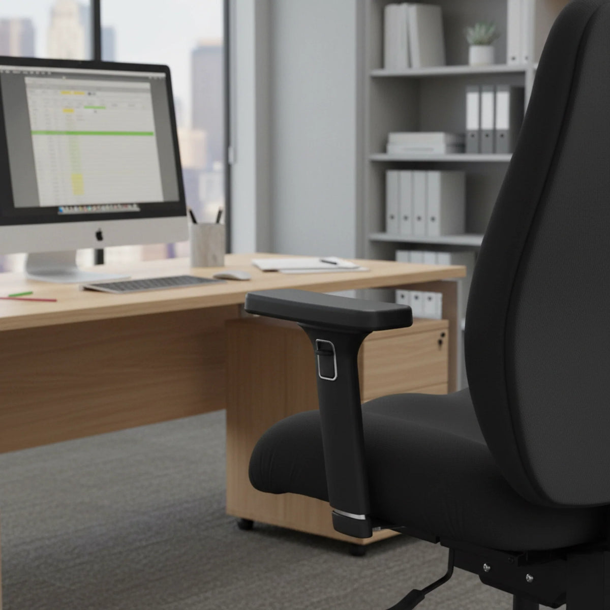 Slika prikazuje ergonomsku uredsku stolicu, točnije model Hercules. Stolica je dizajnirana za udobnost i potporu, prikazujući elegantan crni dizajn s podstavljenim sjedalom i podesivim naslonima za ruke. U pozadini se nalazi moderno uredsko okruženje s radnim stolom, računalom i organiziranim policama, stvarajući profesionalnu atmosferu radnog prostora.