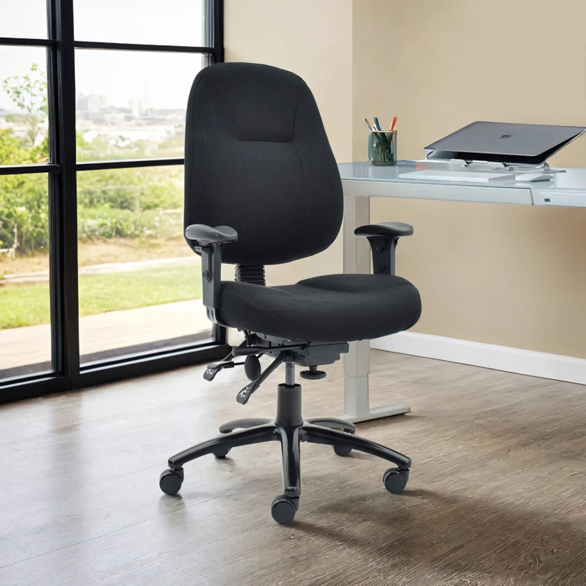Proizvod je ergonomska uredska stolica, točnije model Max Pro. Stolica ima crne presvlake od tkanine, podesive naslone za ruke i sjedalo podesivo po visini. Pozicionirana je u modernom uredskom okruženju s radnim stolom i velikim prozorom u pozadini, omogućujući prirodnom svjetlu da osvijetli prostor.