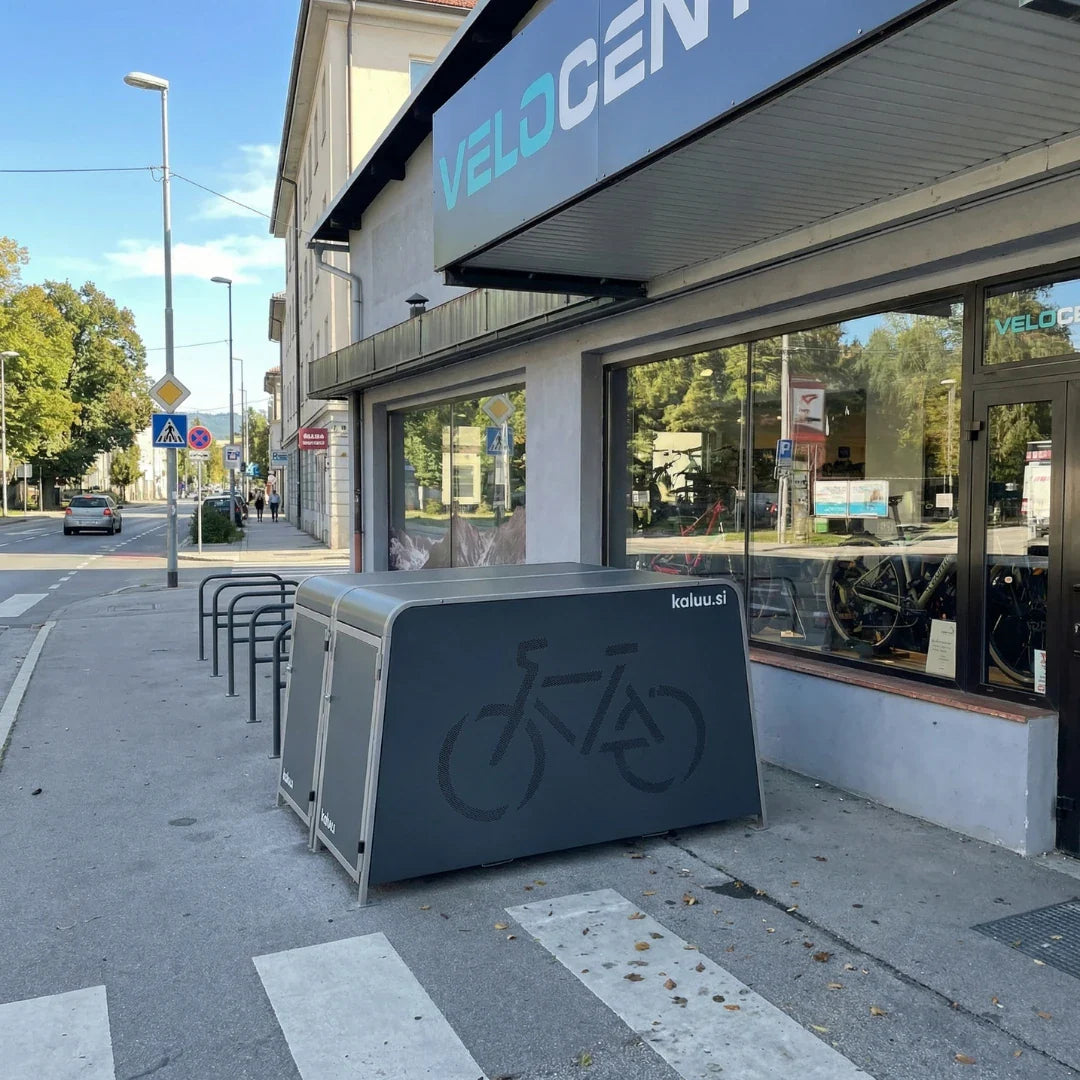 Siva metalna kutija za bicikle Kaluu City Box postavljena ispred trgovine bicikala
